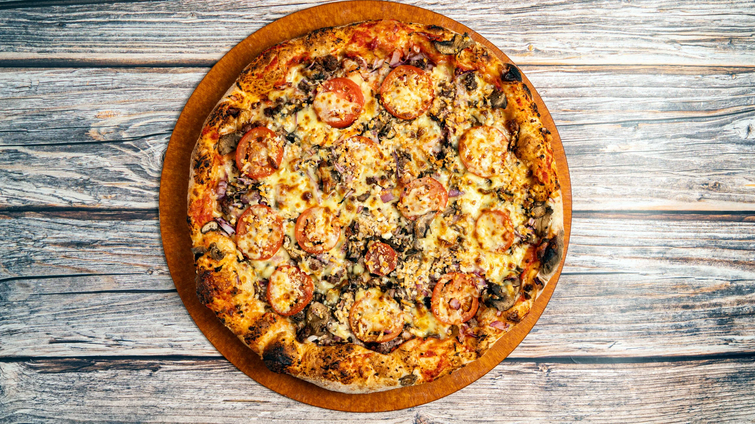 Authentic pizza with ground beef, mushrooms, red onions, tomatoes and feta on a wooden table